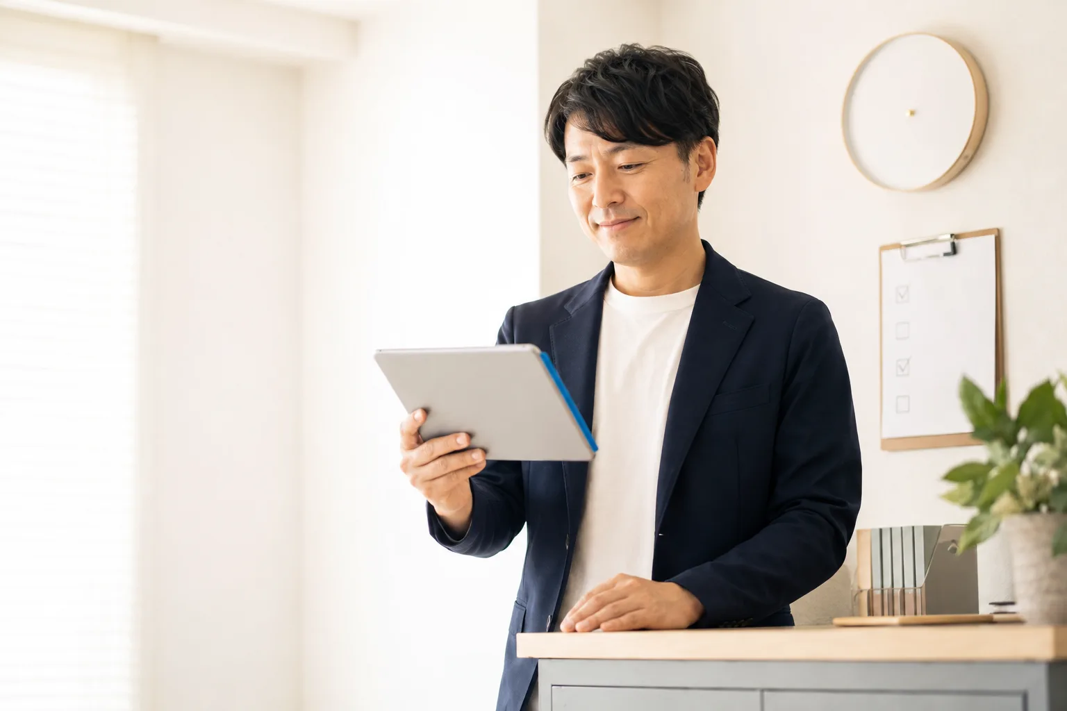 壁掛け時計とチェックリストのあるカウンターでタブレットを確認するスタッフ
